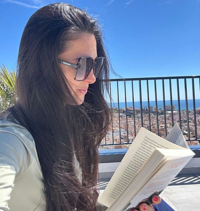 Aitekin Bertelsen liest auf einer Terrasse mit Blick auf Málaga und das Meer