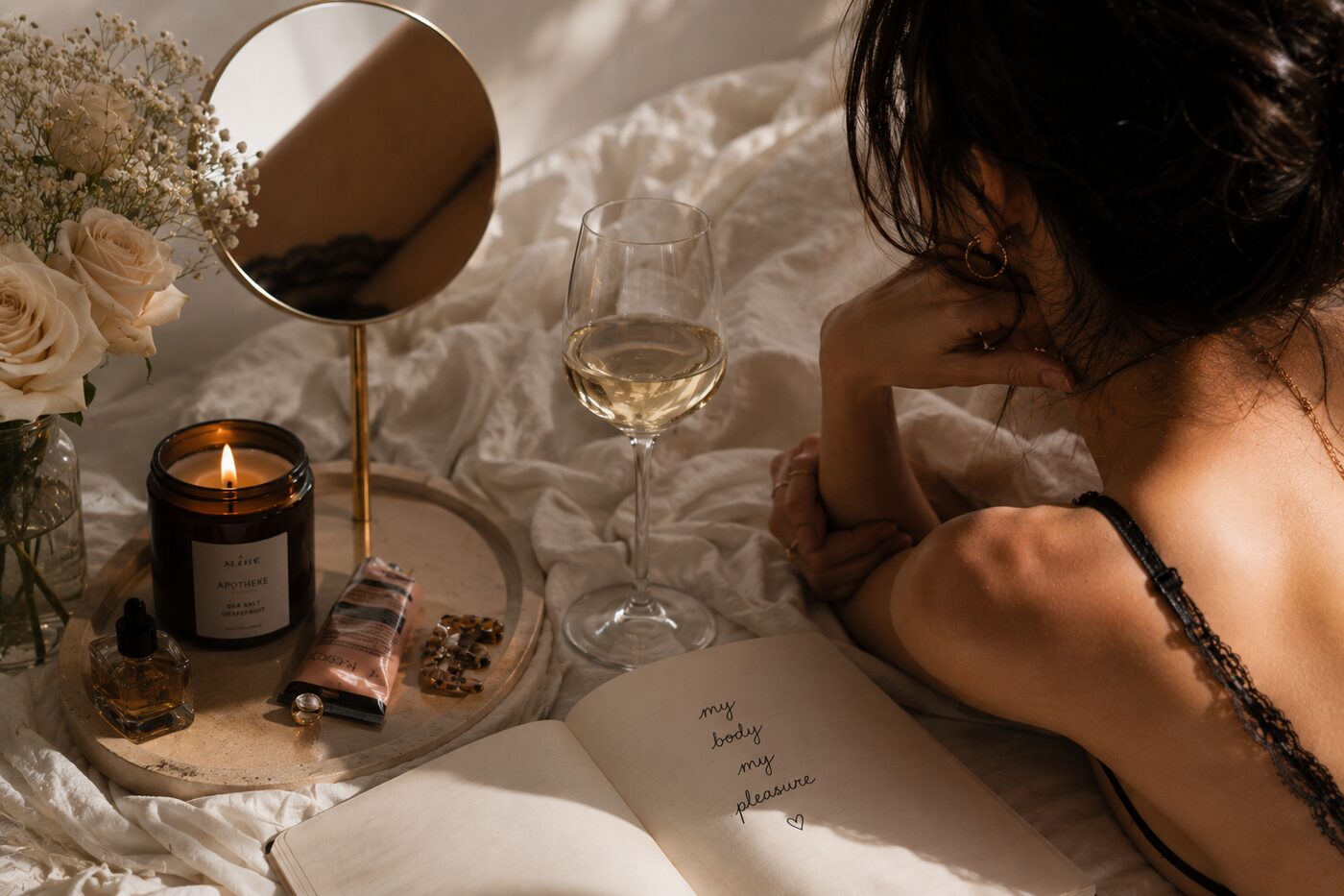 Frau liegt im Bett bei Kerzenlicht, daneben ein Glas Wein und ein Tagebuch mit den Worten „my body my pleasure