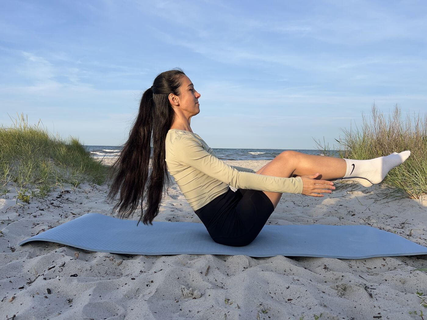 Aitekin in Boot-Pose (Navasana) am Strand mit angehobenen Beinen und Händen an den Knien